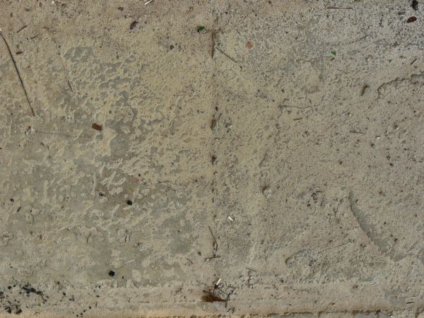 Concrete ground texture in grey and beige tones with very rough, worn surface.