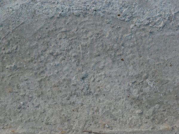 Concrete floor texture in light grey tone with very rough, inconsistent surface and brown dirt.