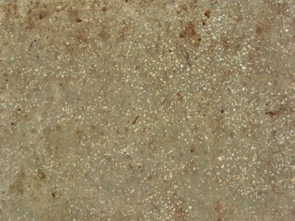 Worn concrete ground texture in brown color with small, jagged rocks embedded in surface.