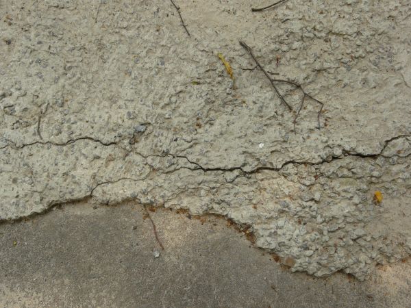 Concrete ground texture in light grey tone with extremely damaged surface and cracks.