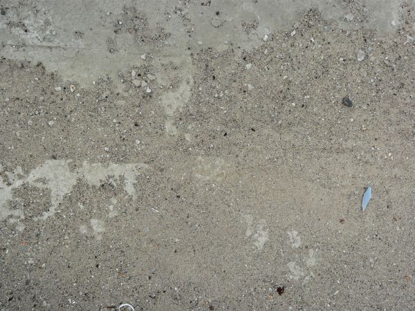 Concrete ground texture in light grey tone with very rough, crumbling surface and thin gravel.