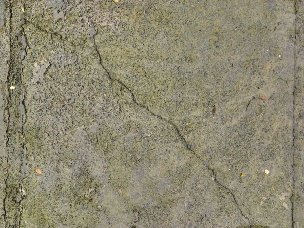 Rough concrete ground texture in grey tone with cracks and dark stains on surface.