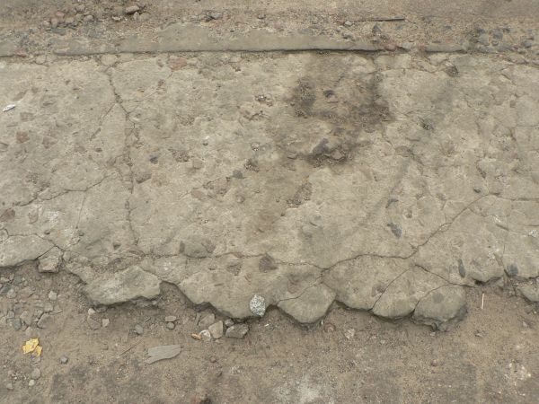 Worn concrete ground texture in light beige tone with very damaged, crumbling surface.