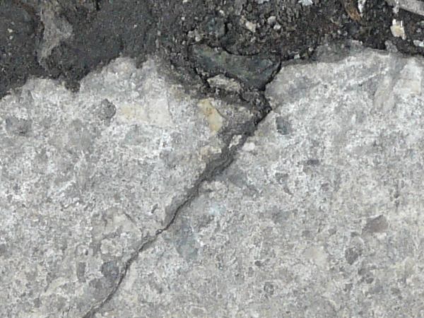 Concrete floor texture in light grey tone with very damaged, cracked surface.
