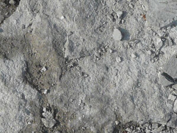 Concrete ground texture in light grey tone with extremely damaged, crumbling consistency.