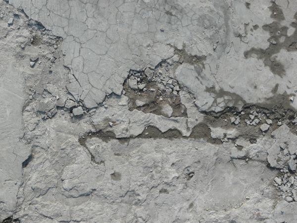 Concrete ground texture in light grey tone with extremely damaged, crumbling consistency.