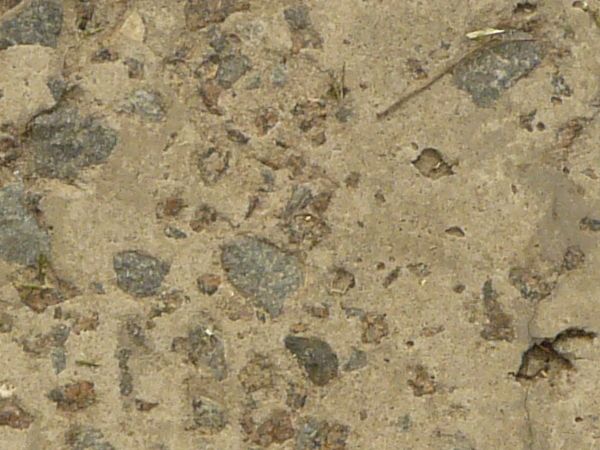 Texture of concrete ground in light beige tone with grey rocks embedded in surface.
