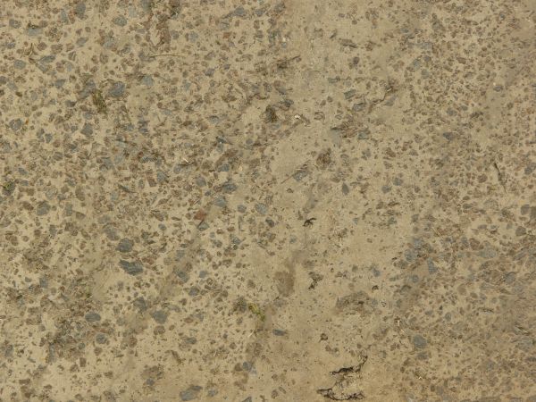 Texture of concrete ground in light beige tone with grey rocks embedded in surface.