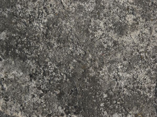 Concrete ground texture in dark grey tone with very rough, damaged surface.