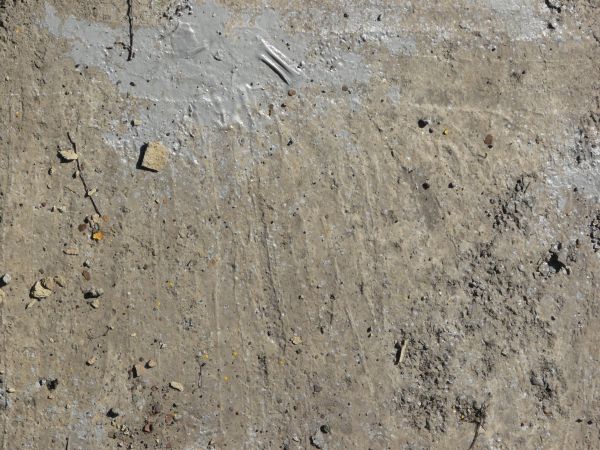 Rugged concrete ground texture with grey paint spot and litter on surface.