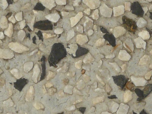 Rough, grey concrete texture with gravel of black and beige tones embedded into surface.