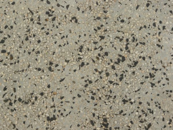 Rough, grey concrete texture with gravel of black and beige tones embedded into surface.