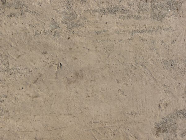 Concrete ground texture in beige and grey tones with rough, inconsistent surface and few, small cracks.