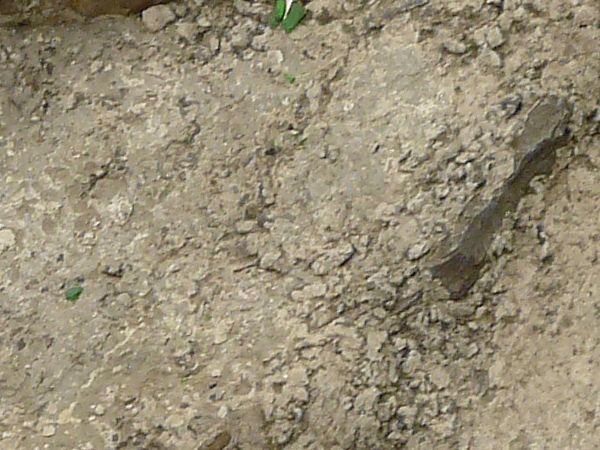 Ground of light brown concrete with extremely damaged, irregular surface and large stones.