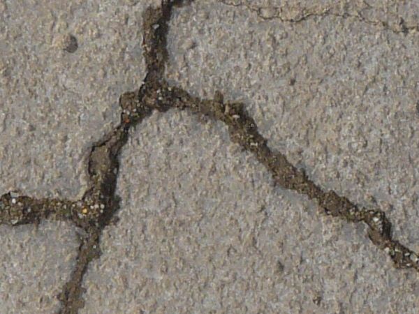 Texture consisting of concrete in light grey tone with rough surface and cracks throughout.