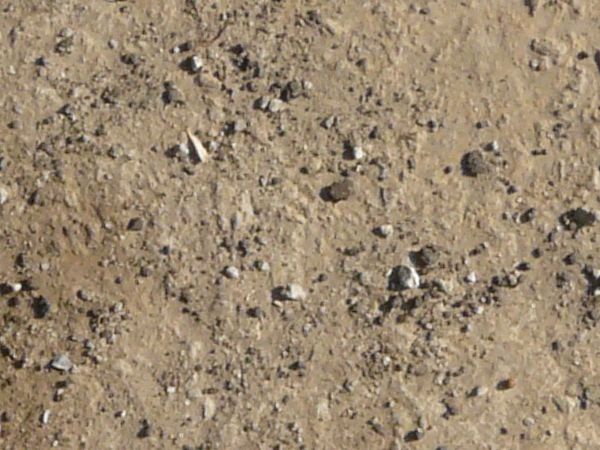 Concrete ground texture in beige color with some gravel on surface and large crack.