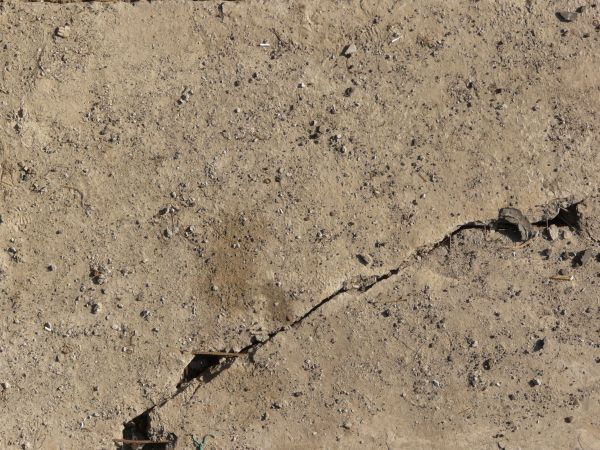 Concrete ground texture in beige color with some gravel on surface and large crack.