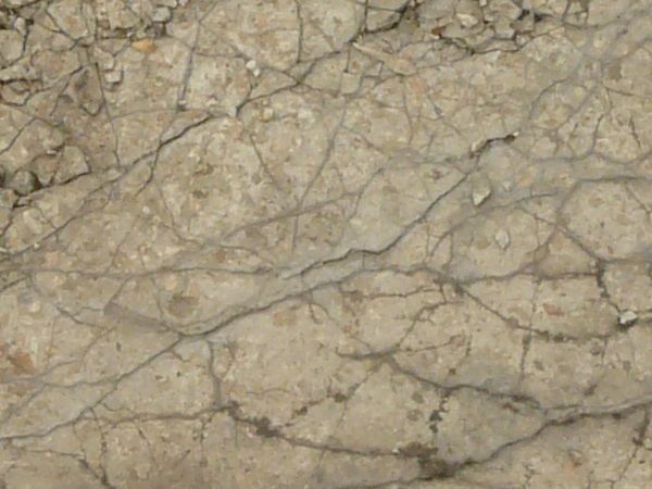 Concrete ground texture in light beige tone with very rough, decrepit surface exposing dirt.