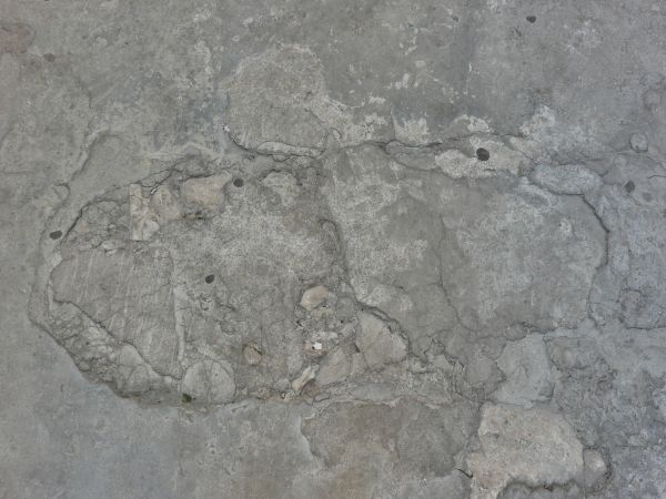 Ground made of concrete in grey tone with irregular surface and cracks.