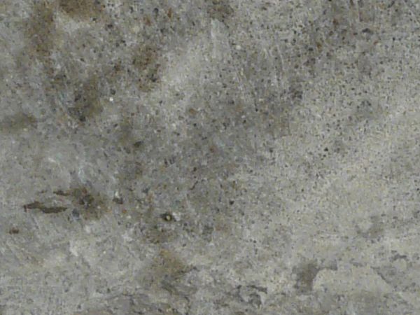 Flat concrete texture in grey tones with random, dark spots across surface.