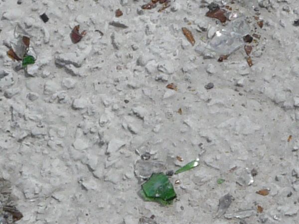 Concrete ground texture with rough surface and myriads of broken, glass bottles.