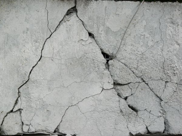 Concrete texture in white tone with very rough surface and large, deep cracks.