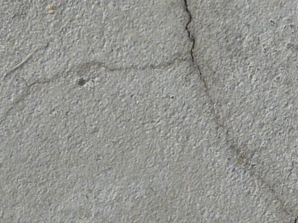 Concrete texture in light grey color with few, thin cracks in rough surface.