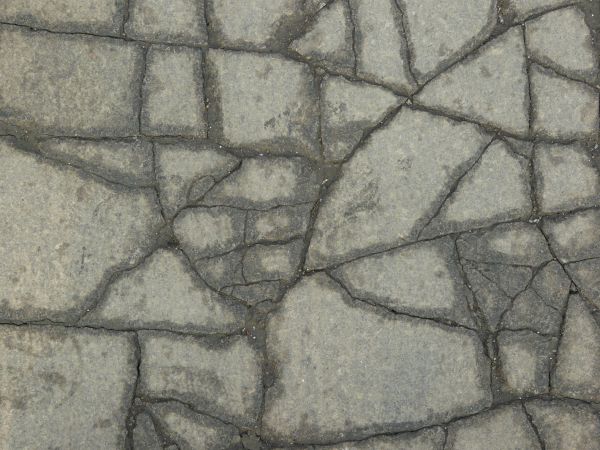 Texture of concrete in grey tone with large, dark cracks in surface.