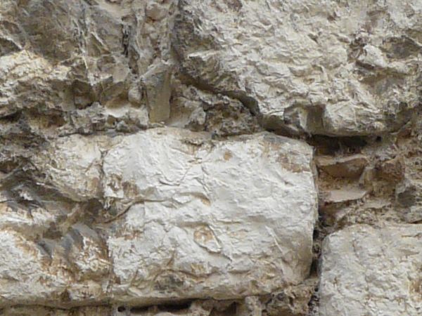 Brick wall with very worn surface covered in thin layer of grey, crumbling concrete.