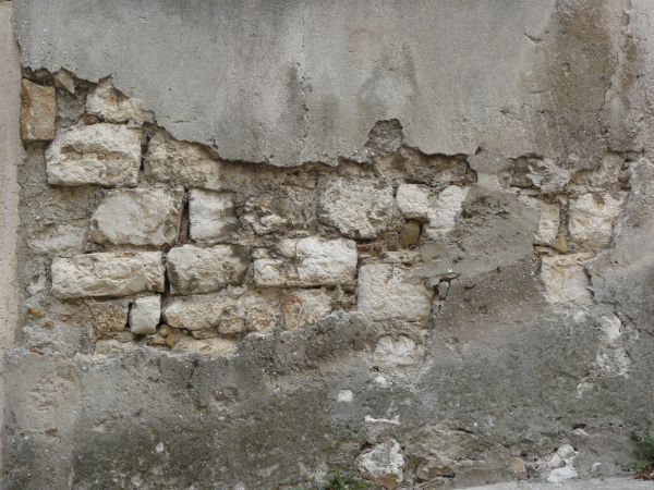 Brick wall with very worn surface covered in thin layer of grey, crumbling concrete.