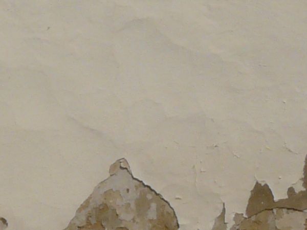 Concrete wall covered in thin layer of pealing, cream-colored stucco.