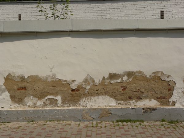 Concrete wall covered in thin layer of pealing, cream-colored stucco.