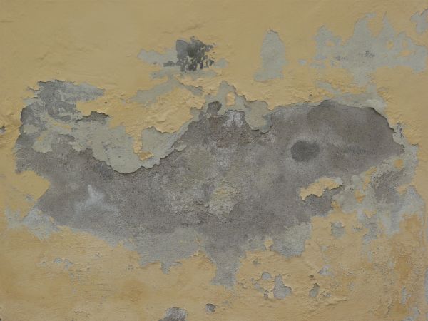 Old wall of concrete covered in thin layer of old, pealing paint in beige tone.