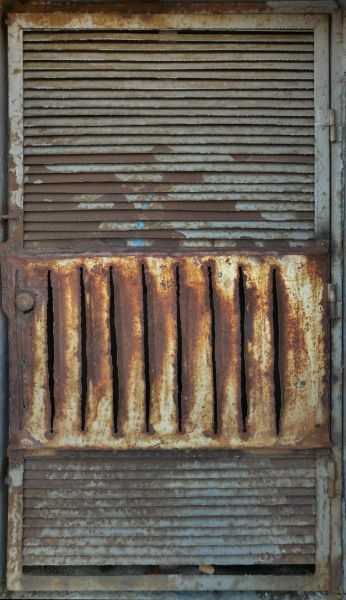 Old metal texture containing vented, metal door with very worn, rusting surface.