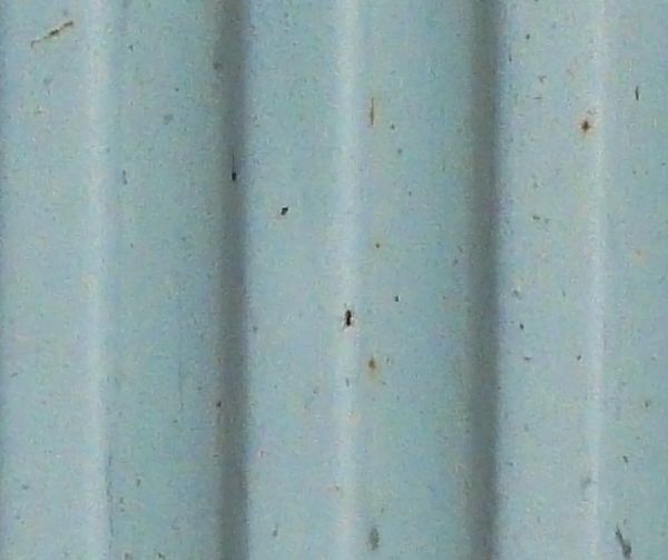 Aged metal siding in light blue color with lined texture and rusting surface.