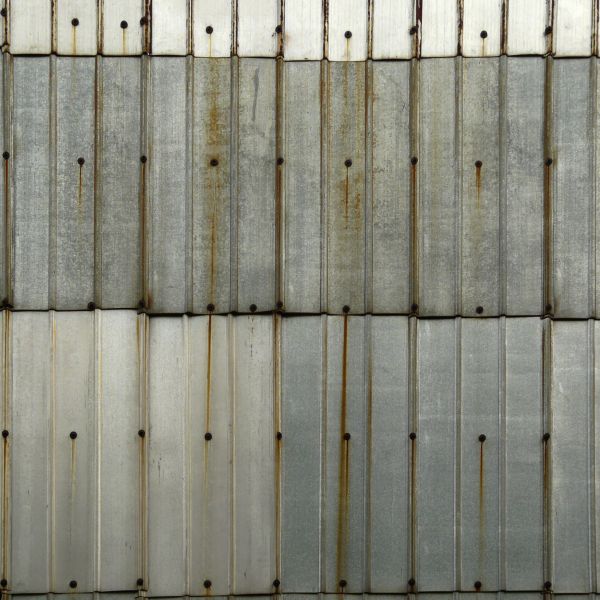 Aluminum sheet metal panels with lined texture and streaks of rust coming from nails.