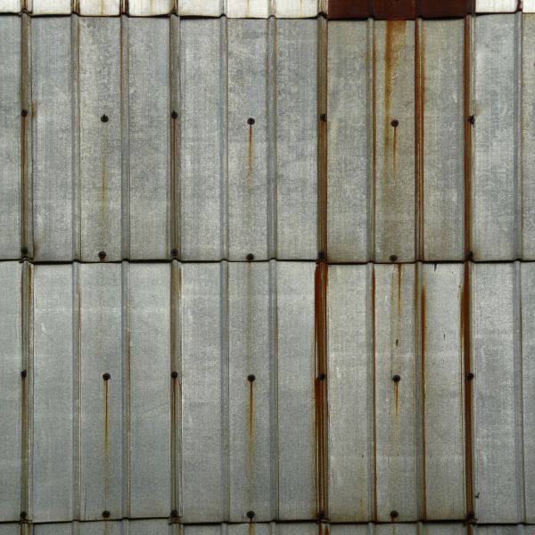 Aluminum sheet metal panels with lined texture and streaks of rust coming from nails.