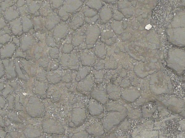 Old cracked rubber in light grey color with gravel in cracks.