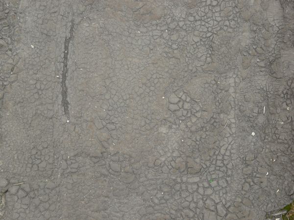 Old cracked rubber in light grey color with gravel in cracks.