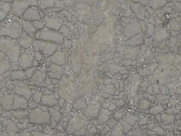 Old cracked rubber in light grey color with gravel in cracks.