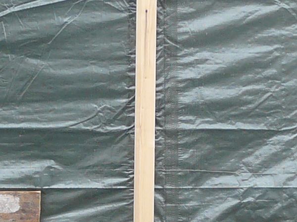 Plastic tarp in dark green tone with wooden planks covering structure.