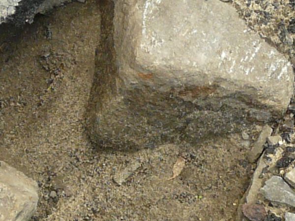 Road texture, broken completely into large and small chips of asphalt, with light, sandy earth and dark rock visible underneath.