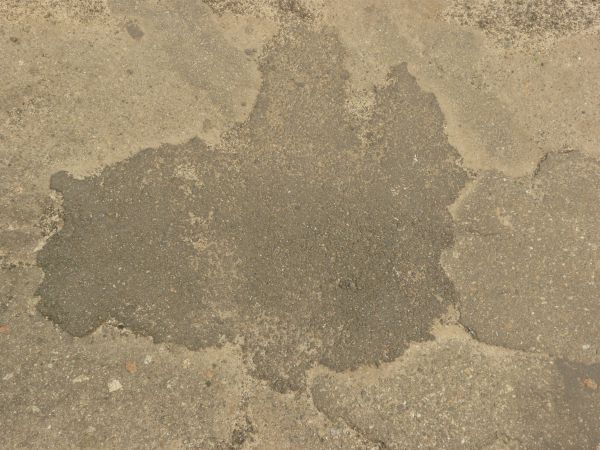 Road texture, sandy brown in color, with a large, irregularly shaped patch of dark asphalt on the center.