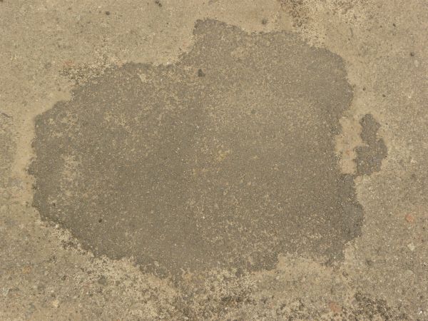 Road texture, sandy brown in color, with a large, irregularly shaped patch of dark asphalt on the center.