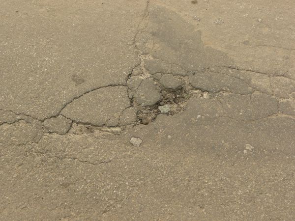 Road texture, brown in color, with a small hole worn into the center with crumbling rock and thin cracks surrounding it.