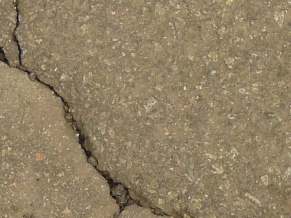 Road texture, brown in color, with a small hole worn into the center with crumbling rock and thin cracks surrounding it.