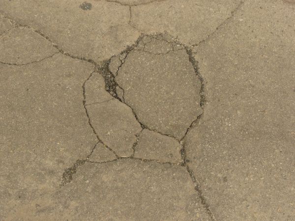 Road texture, brown in color, with a small hole worn into the center with crumbling rock and thin cracks surrounding it.