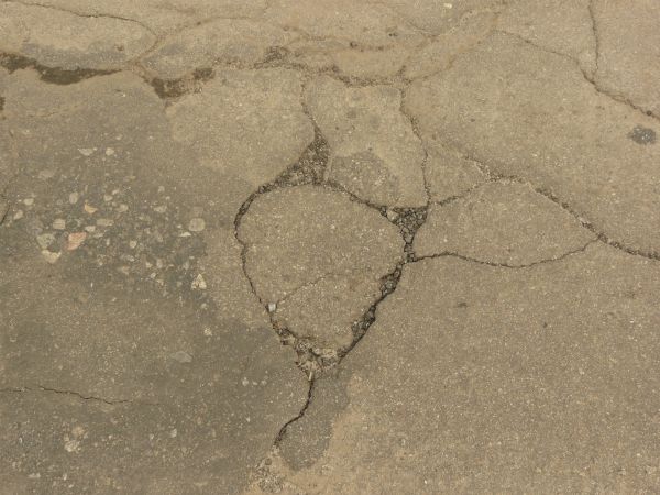 Road texture, brown in color, with a small hole worn into the center with crumbling rock and thin cracks surrounding it.