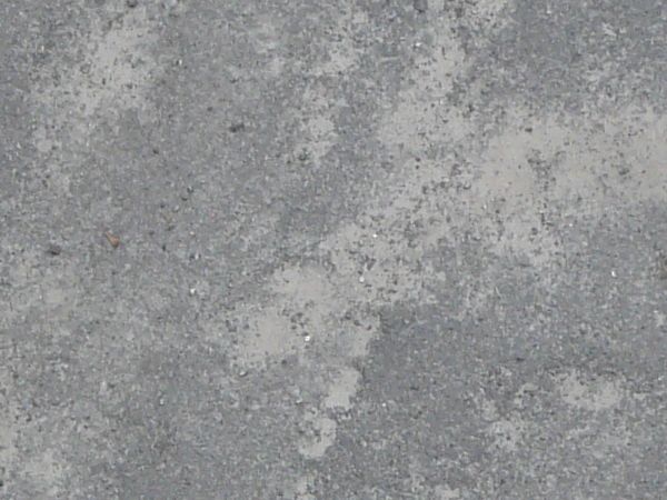 Road texture, uneven and in varying shades of grey, with significant cracks, crumbling, areas of fine dust and small green weeds.