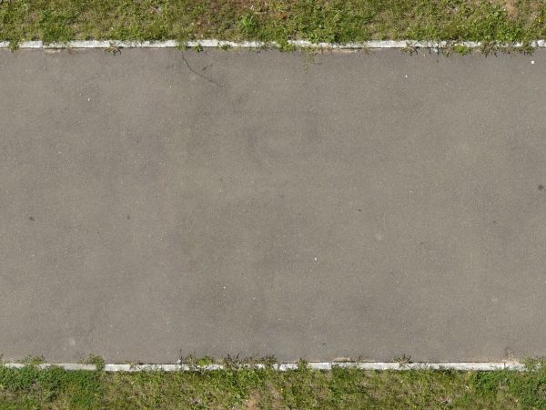 Texture of new, asphalt road in grey tone with grass at edges.